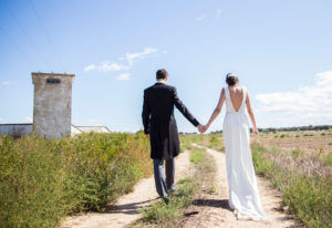 Novios de espaldas y cogidos de la mano caminando por el campo, reportaje de boda Roberto y Ana por Andrea Aragón.