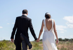 Plano corto de los novios de espaldas y cogidos de la mano caminando por el campo, reportaje de boda Roberto y Ana por Andrea Aragón.