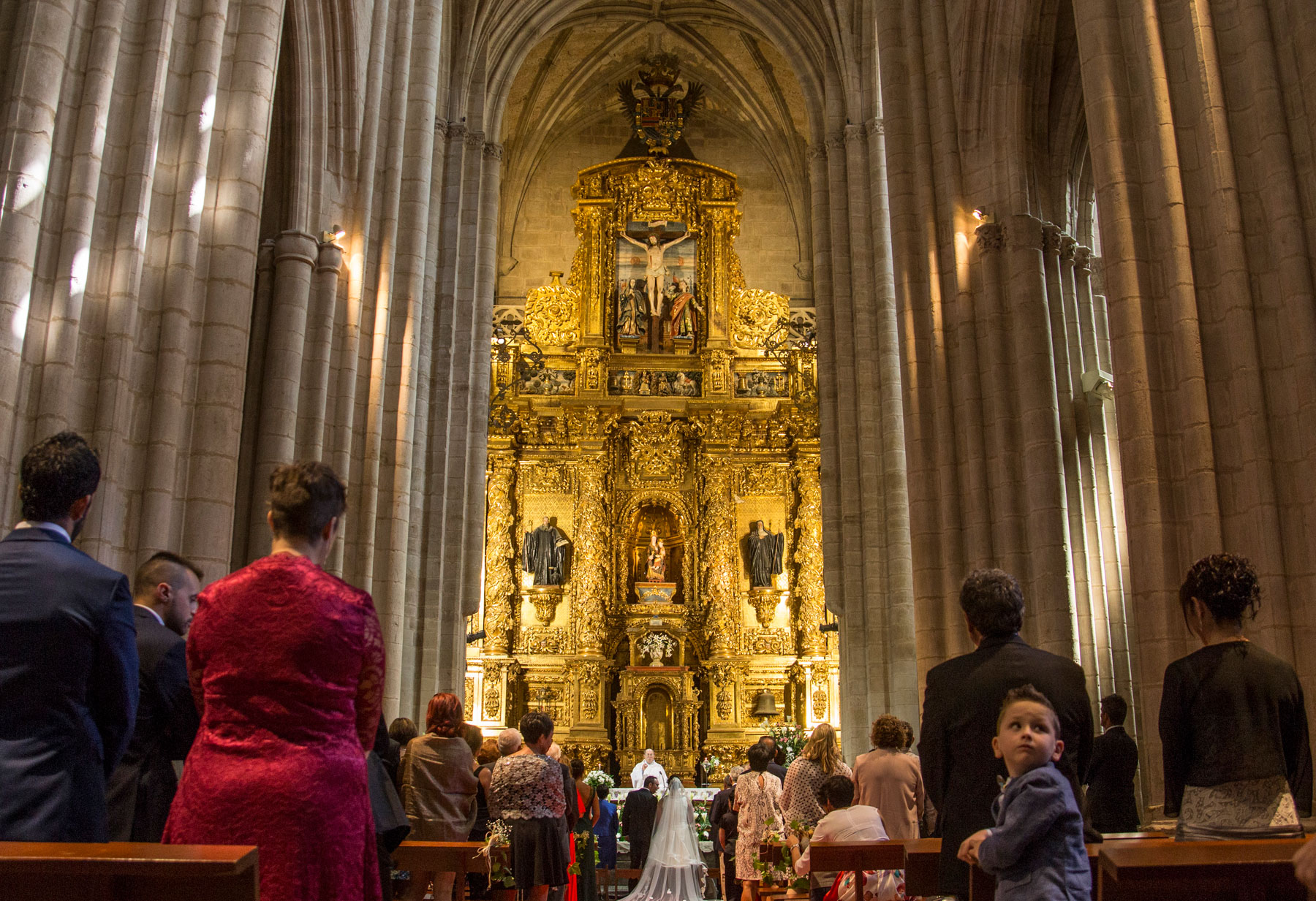 Interior del Monasterio de Santa María la Real de Nájera con novios e invitados de espaldas, de frente, espectacular retablo. Reportaje de boda Patricia y Miguel por Andrea Aragón.
