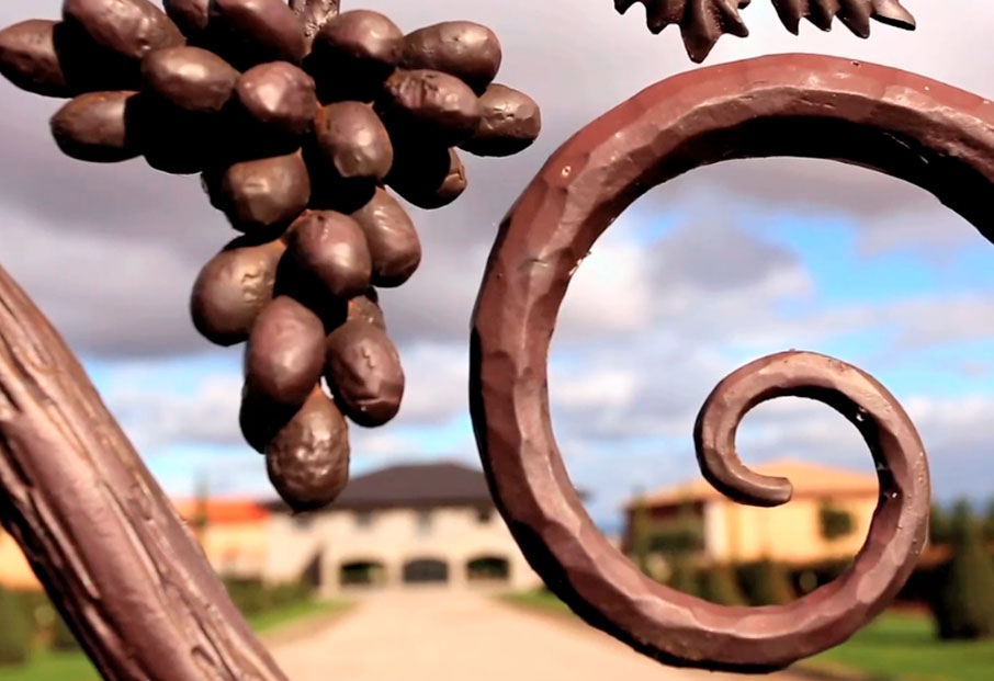 Imagen de detalle de la verja con unas uvas y de fondo la bodega. Bodega Señorío de Villarrica pertenece a una familia de viticultores y bodegueros de la D.O.Ca. Rioja, asentados tradicionalmente en el corazón de la Rioja Alta, en San Asensio y con bodega en Hervías. Reportaje de Andrea Aragón